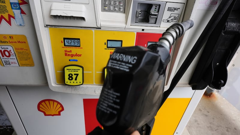 ARCHIVO - Una pantalla muestra el precio del combustible mientras un cliente sostiene una...
